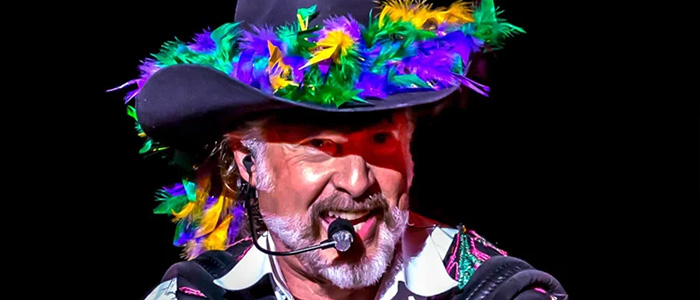 Man with a white beard wearing a colorful purple hat with feathers