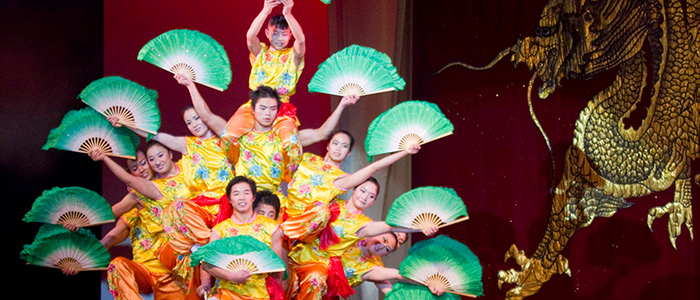 A group of people dressed in yellow and red each hold green fans