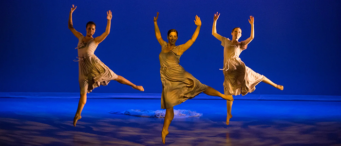 Three dancers performing on stage under blue lighting
