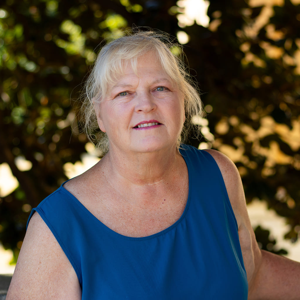 A woman standing in blue shirt in front of a tree