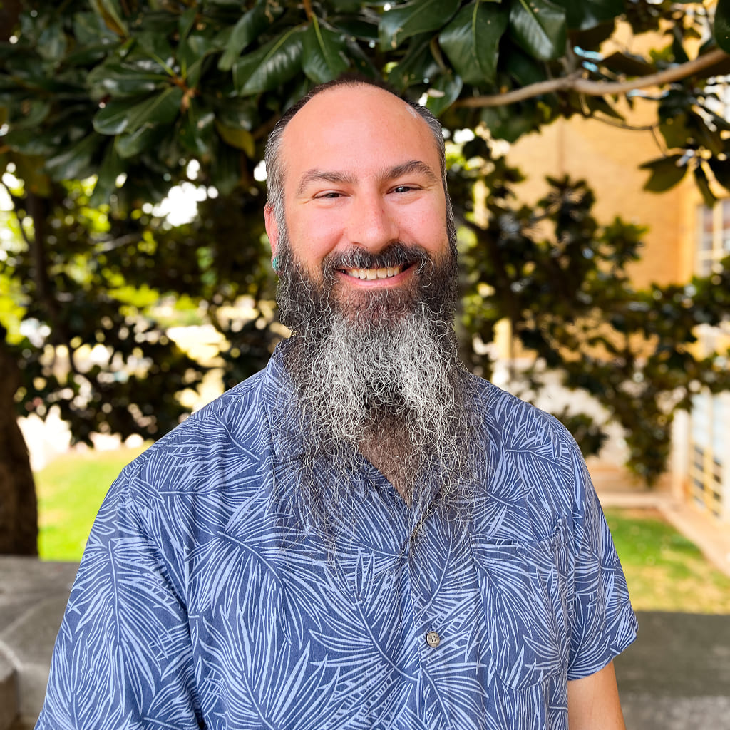 A man in a beautiful blue button up shirt and with long beard smiling