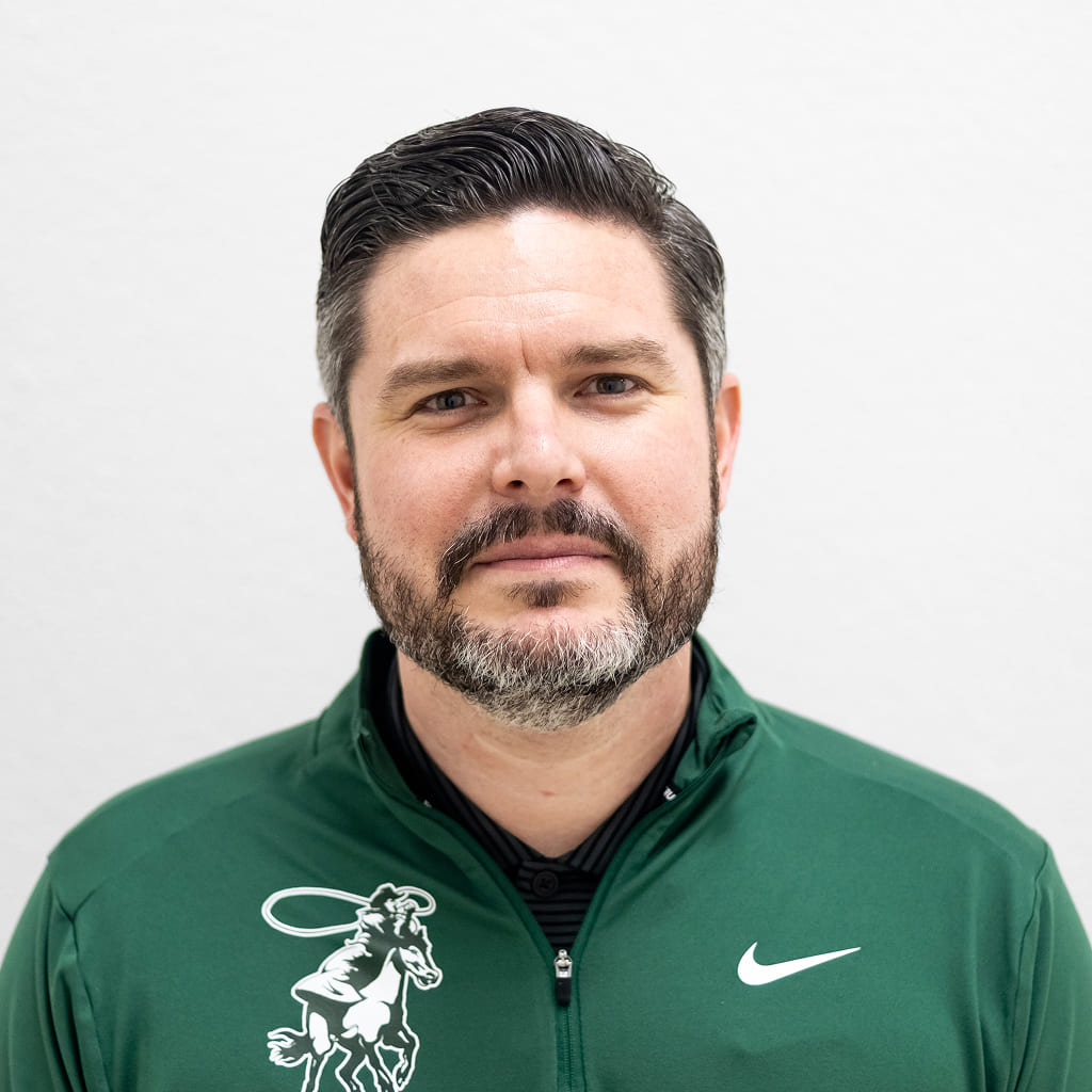 A man with a beard in a green quarter zip-up smiling