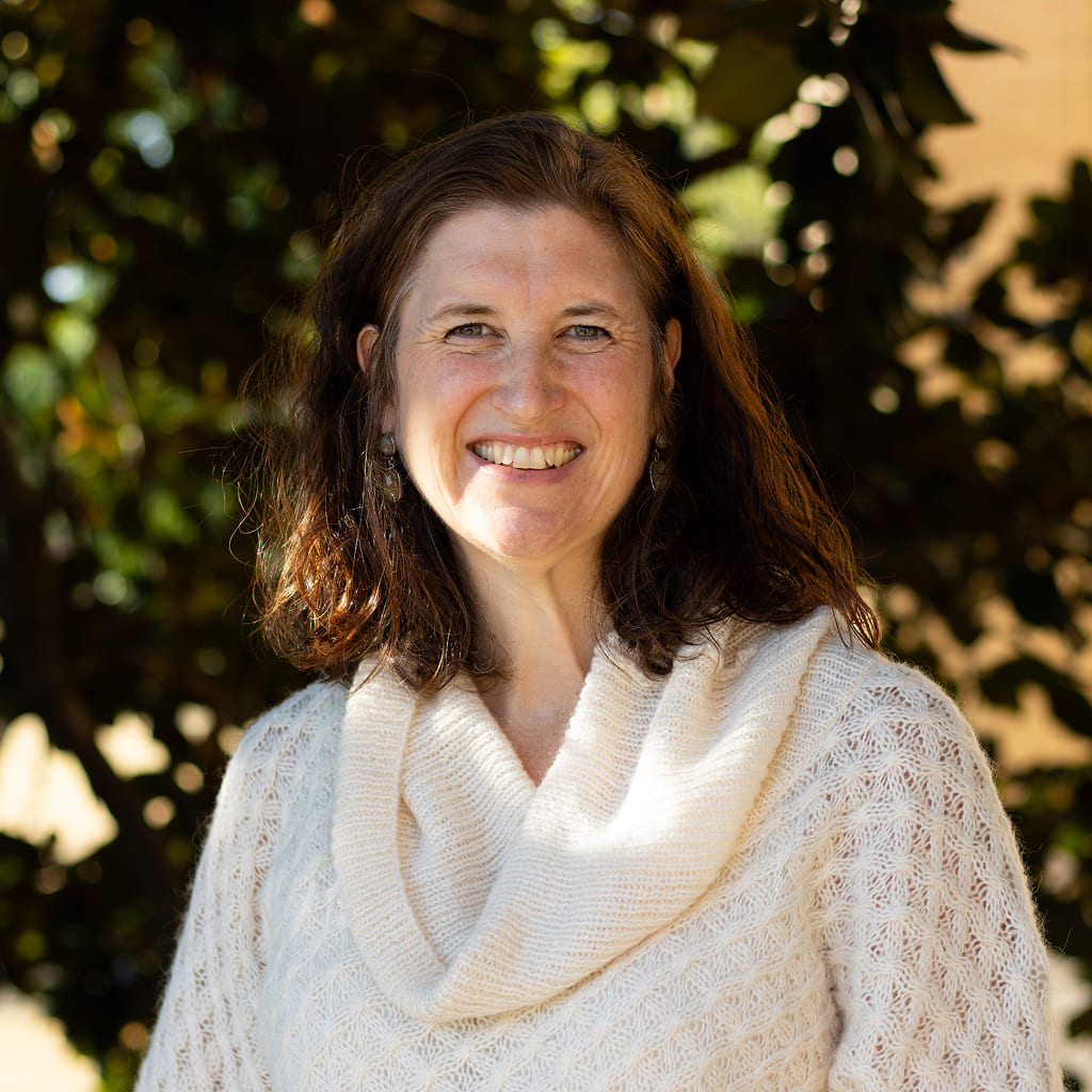 A woman in a white top standing and smiling