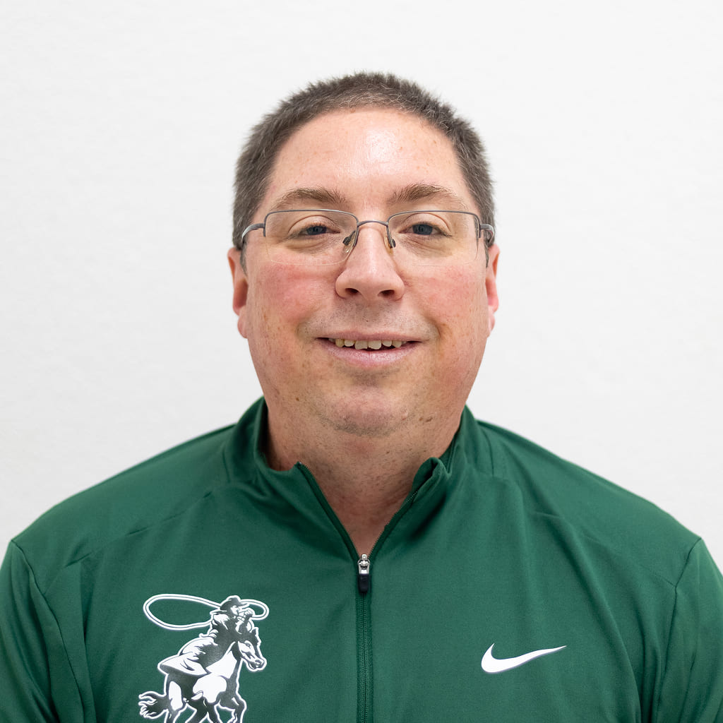 A man in a green quarter zip-up and glasses smiling