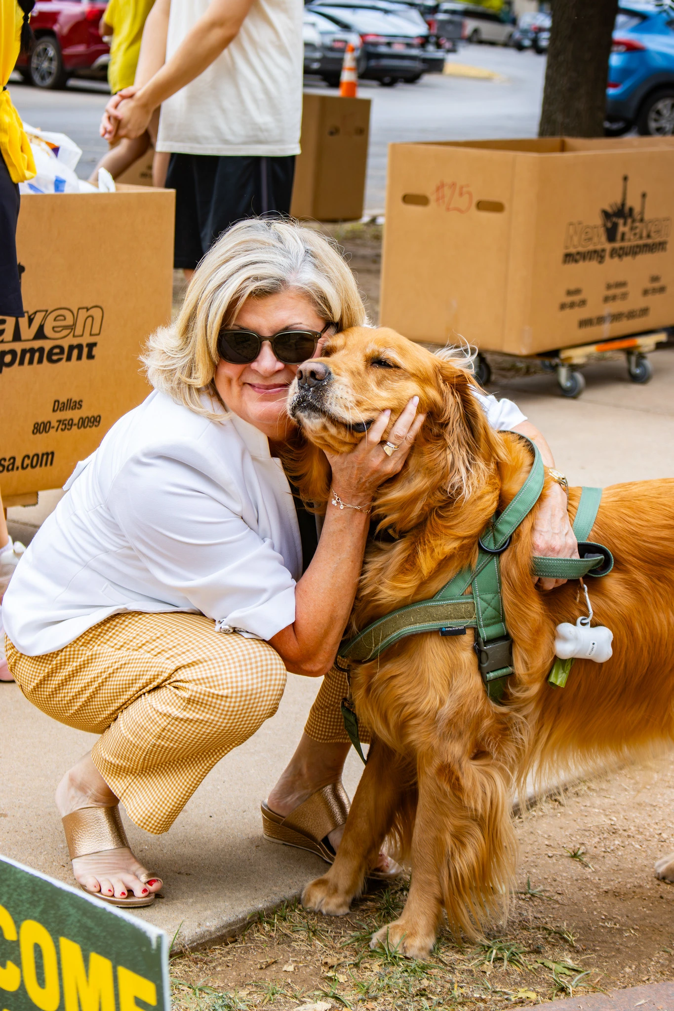 Woman wearing sunglasses hugs a golden retriever during a campus move-in event.